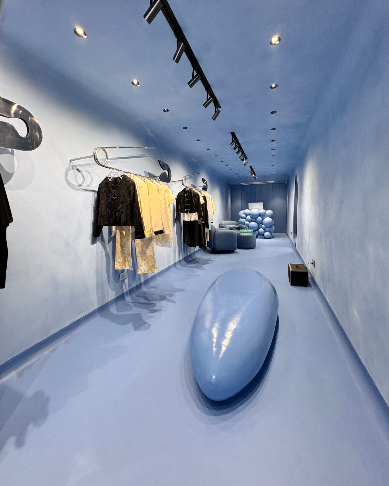 The Hawk & Wolf store in Kala Ghoda: a long blue room with a smooth blue sculptural form in the middle and clothes on safety-pin rails along the wall.