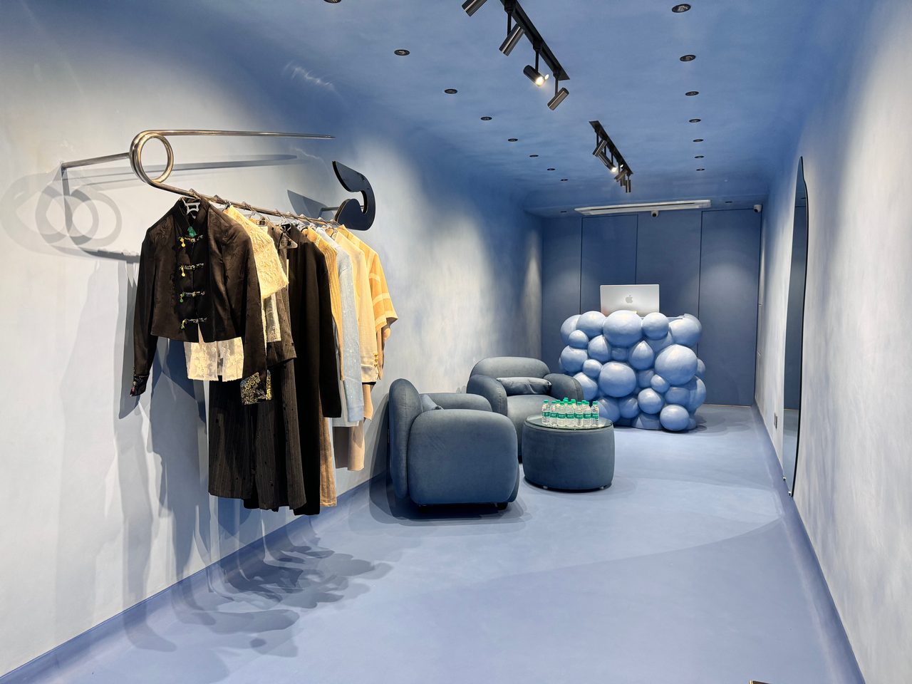 Black and ivory pieces on a safety-pin rail, with blue armchairs and the sphere counter at the back of the store.